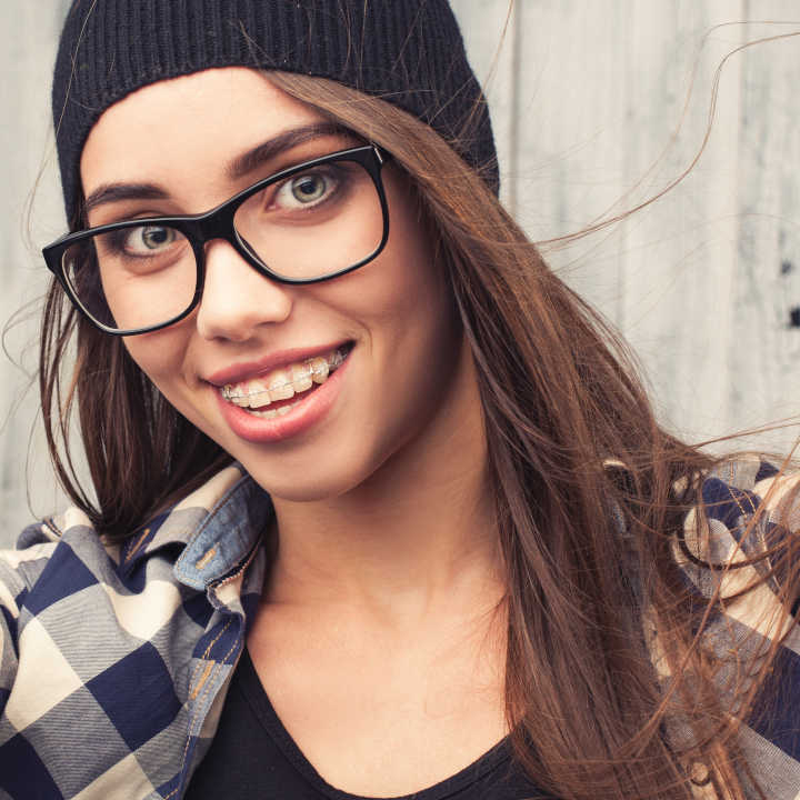smiling Hipster girl in glasses and braces making a selfshoot on wooden background